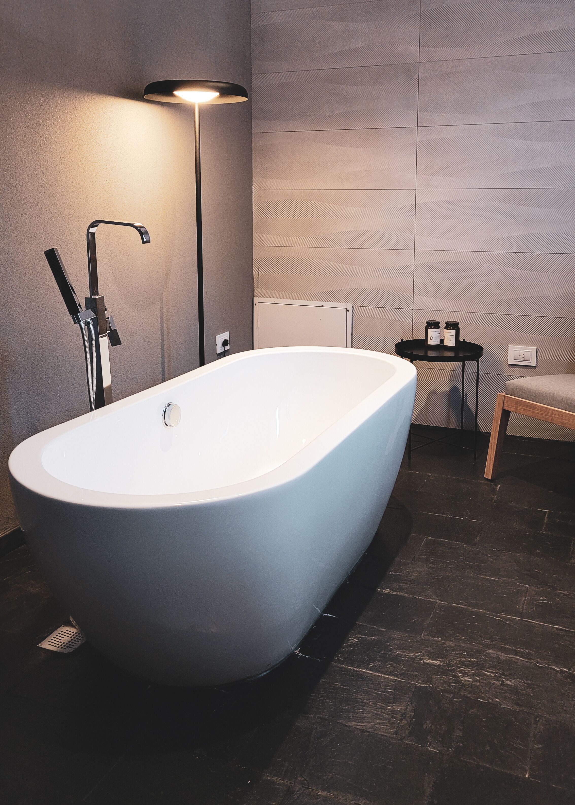 A modern bathroom with a freestanding bathtub, a wall-mounted towel rack, and a small table with candles.