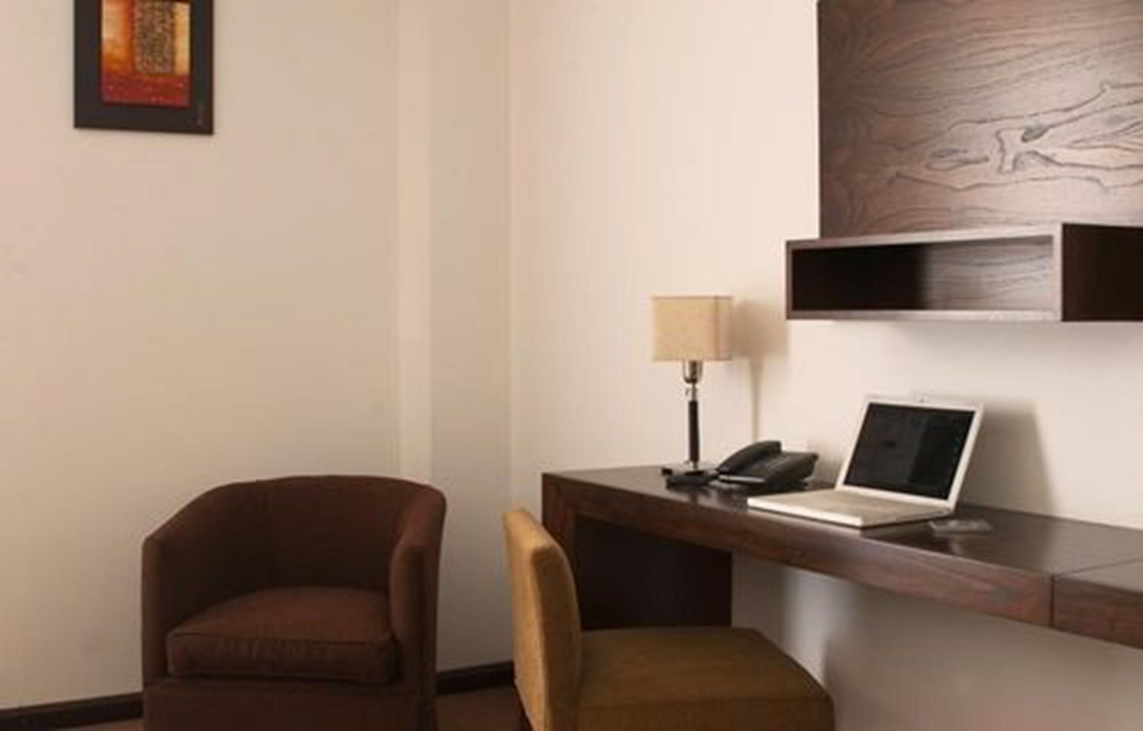 Een hotelkamer met een bureau, een laptop, een lamp en twee stoelen.