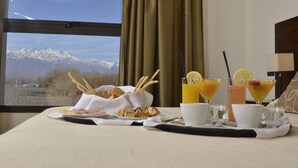 A breakfast tray with croissants, a plate of food, and three drinks on a table with a view of mountains through a window. - Fuente Mayor Hotel And Resort (Tunuyan)