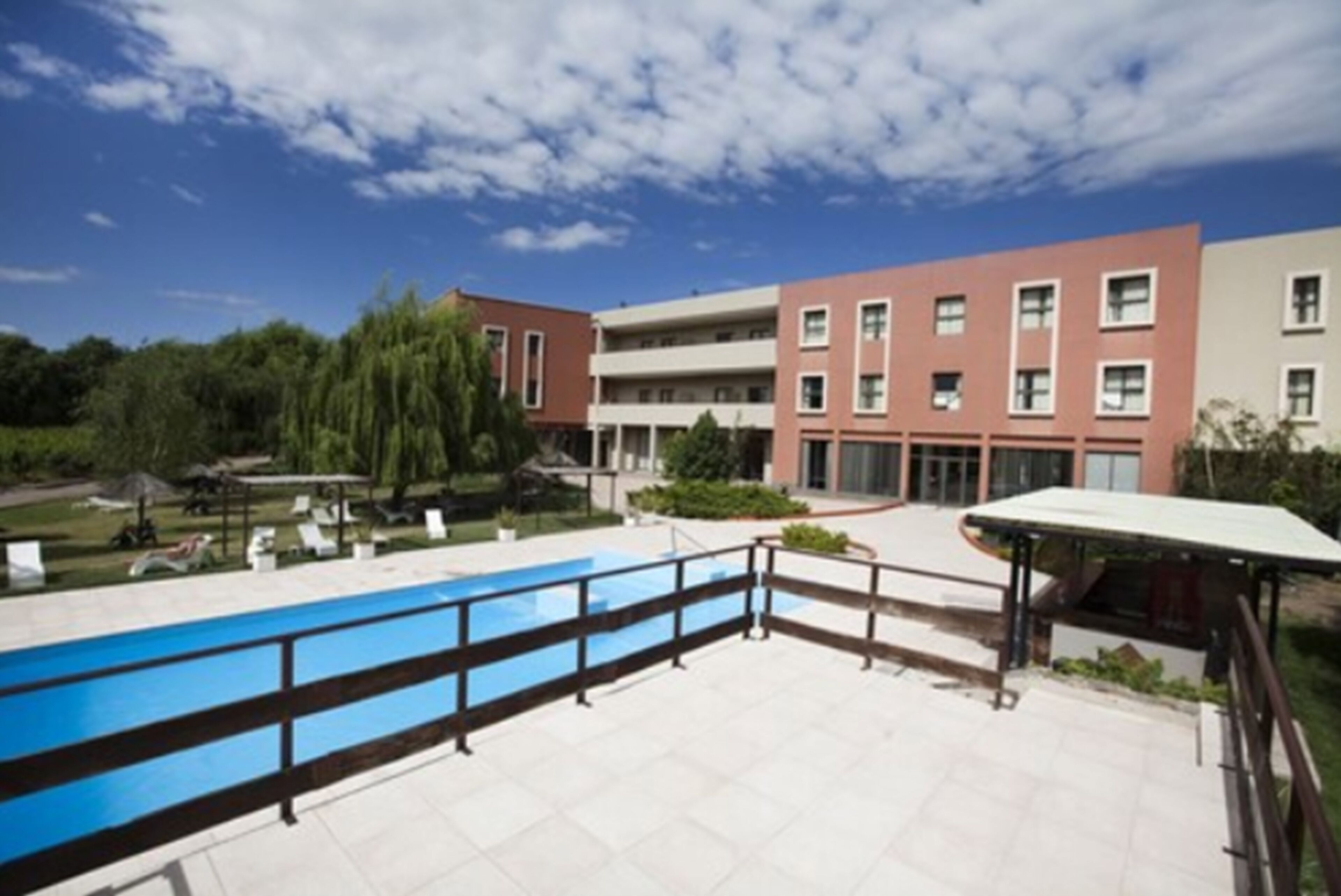 A modern building with a swimming pool, surrounded by greenery and a clear sky.
