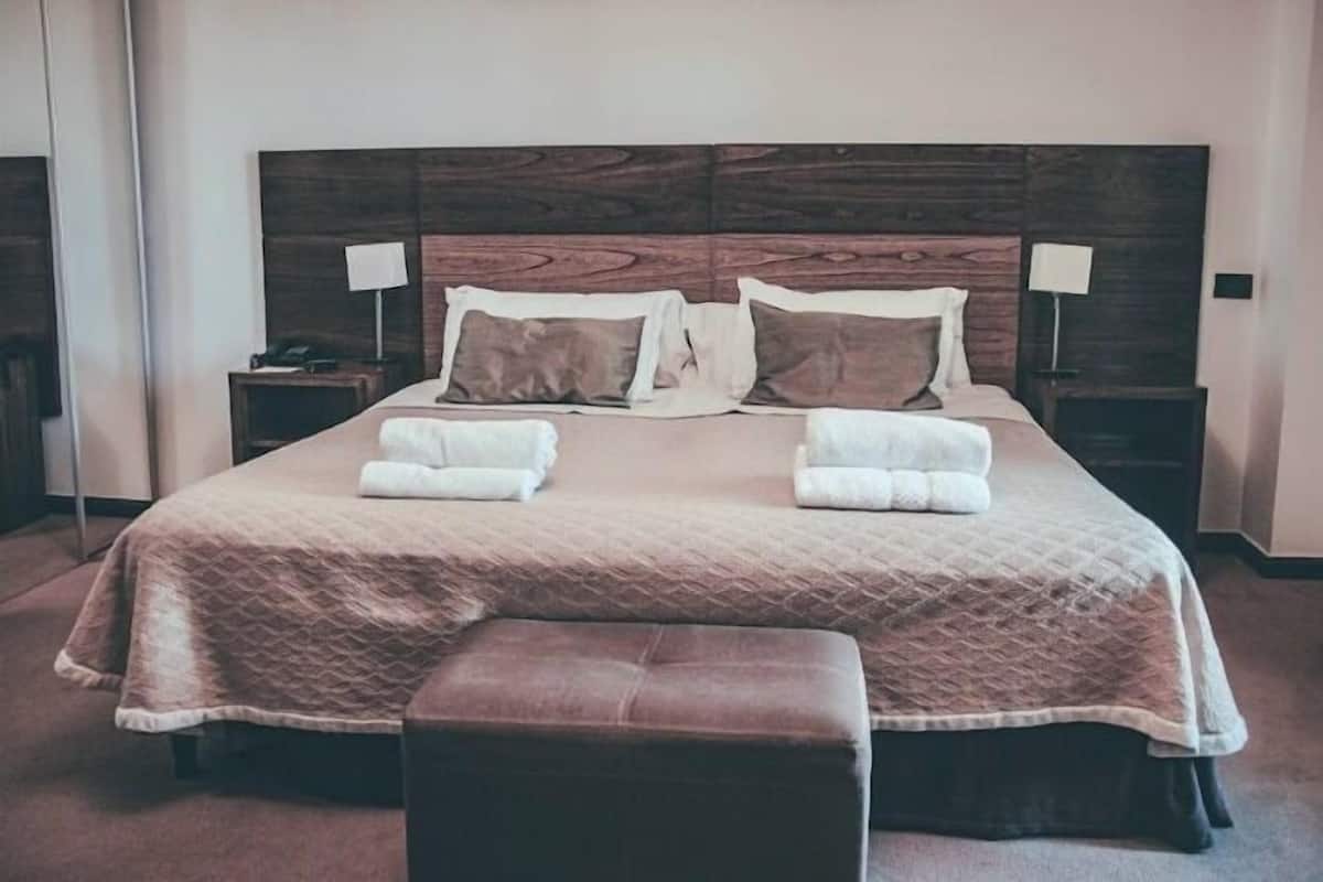 A neatly made bed with a quilted cover, two bedside tables with lamps, and a bench at the foot of the bed.