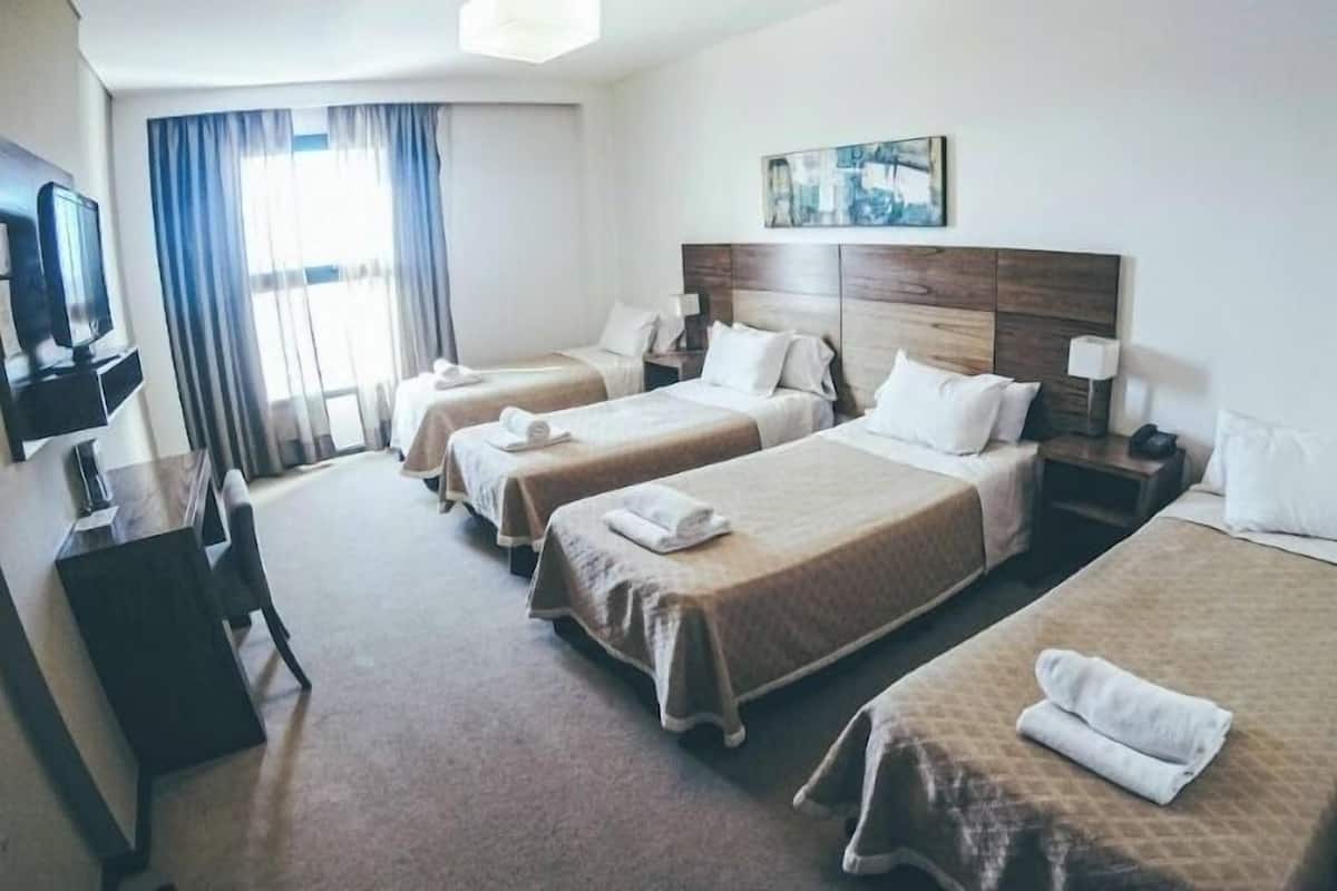 A hotel room with four single beds, a television, a painting on the wall, and a window with curtains.