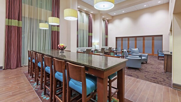 A hotel lobby with a long dining table, blue cushioned chairs, a seating area with sofas, and a reception desk. - Hampton Inn & Suites Shreveport/Bossier City Airline Drive (Bossier City)