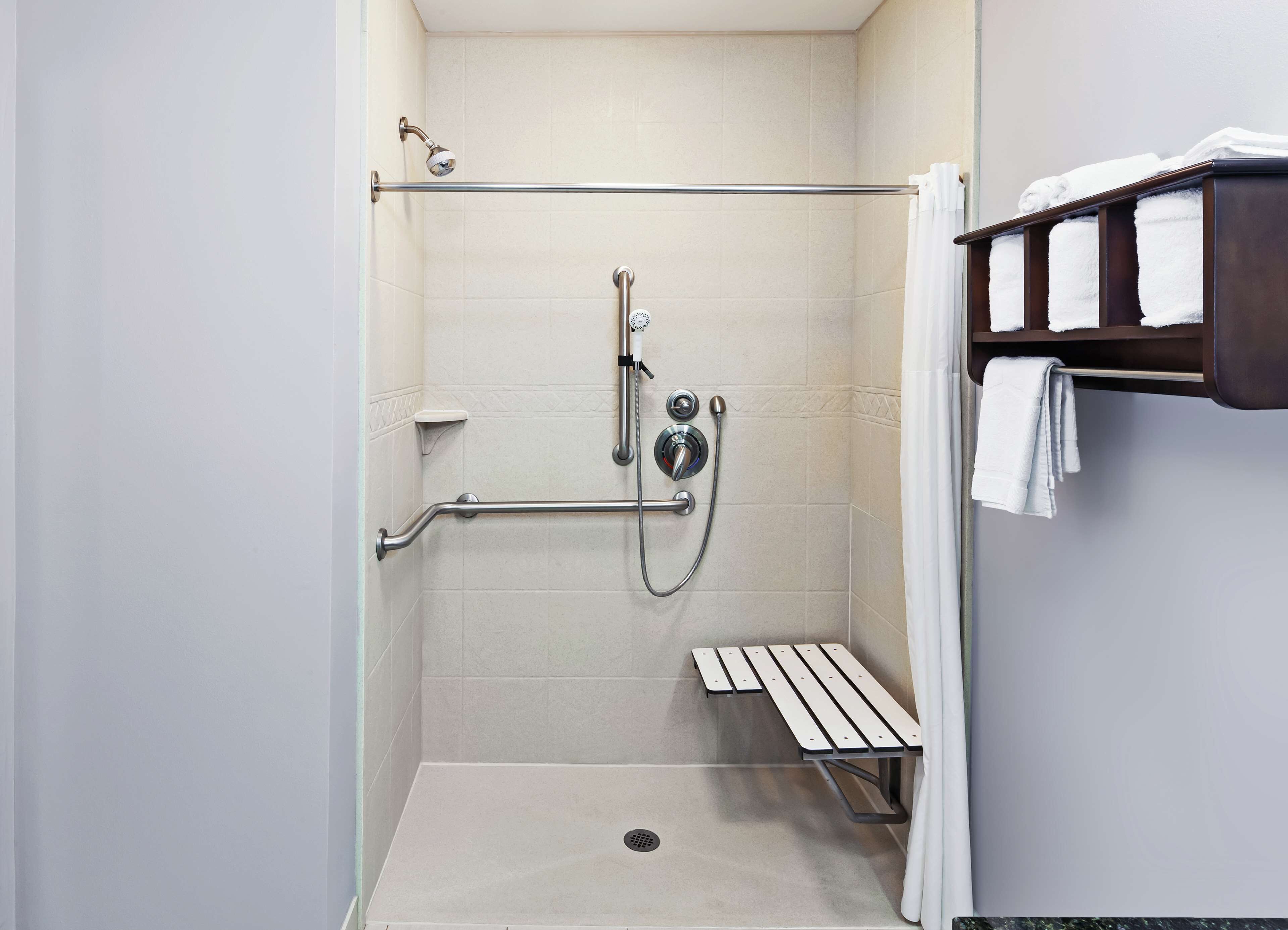 A shower area with a grab bar, a bench, and a towel rack.