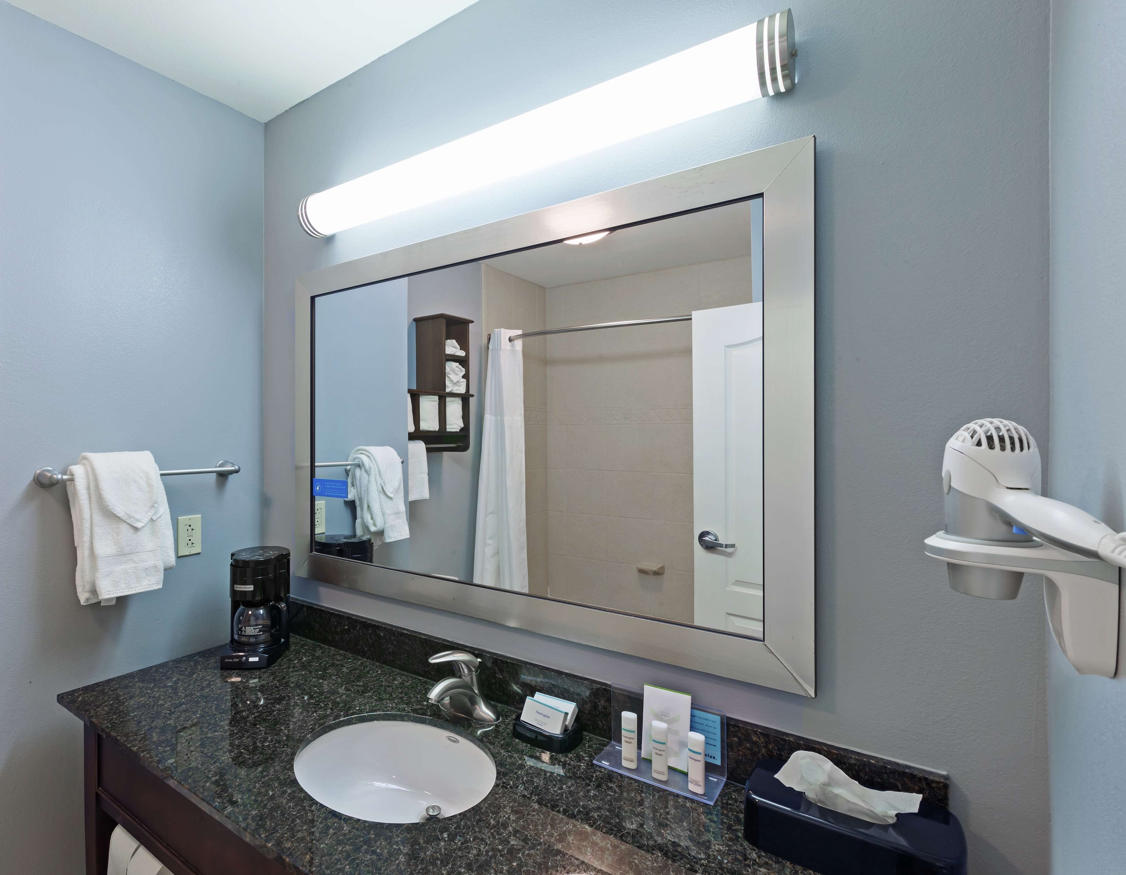 A bathroom with a sink, mirror, towel rack, and a hairdryer on a stand.