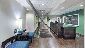 A hotel lobby with a reception desk, a waiting area with chairs, a patterned carpet, and a green wall with a 'happy' sign. - Hampton Inn & Suites Shreveport/Bossier City Airline Drive (Bossier City)