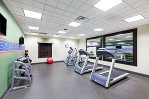 Ein Fitnessstudio mit Laufbändern, Crosstrainern und einem an der Wand montierten Fernseher.