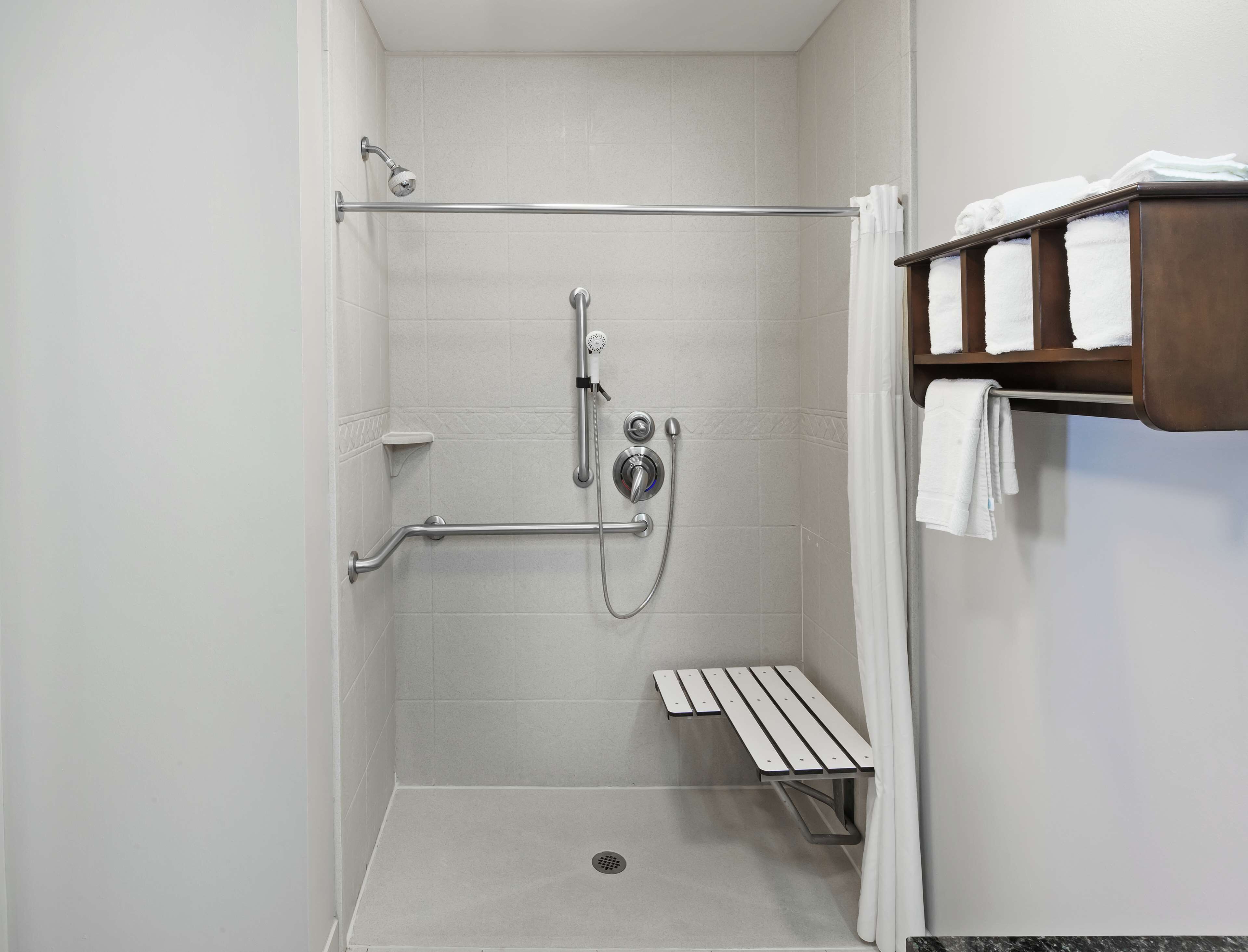A walk-in shower with a grab bar, a bench, and a towel rack.