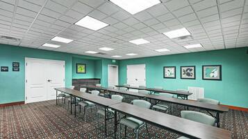 Un salón de conferencias con paredes verde azulado, varias mesas, sillas y una alfombra estampada.