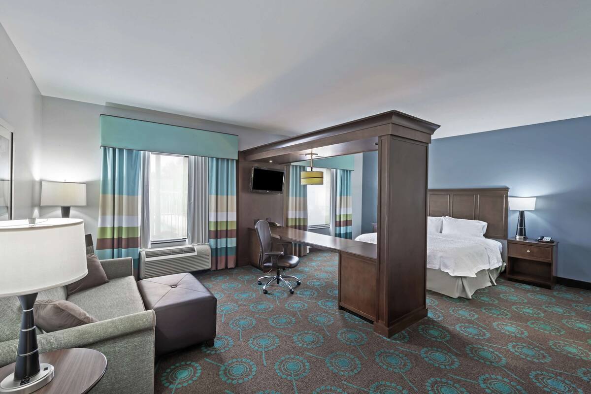 Une chambre d’hôtel avec un lit, un bureau, une chaise, une télévision et un grand miroir.