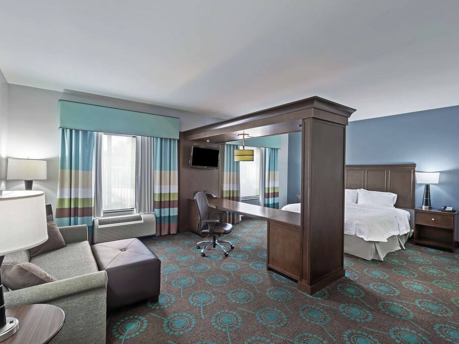 Habitación de hotel con cama, escritorio, silla, televisor y un espejo grande.