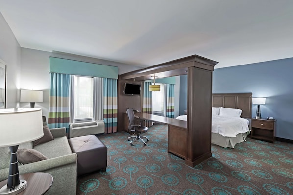 Habitación de hotel con cama, escritorio, silla, televisor y un espejo grande.
