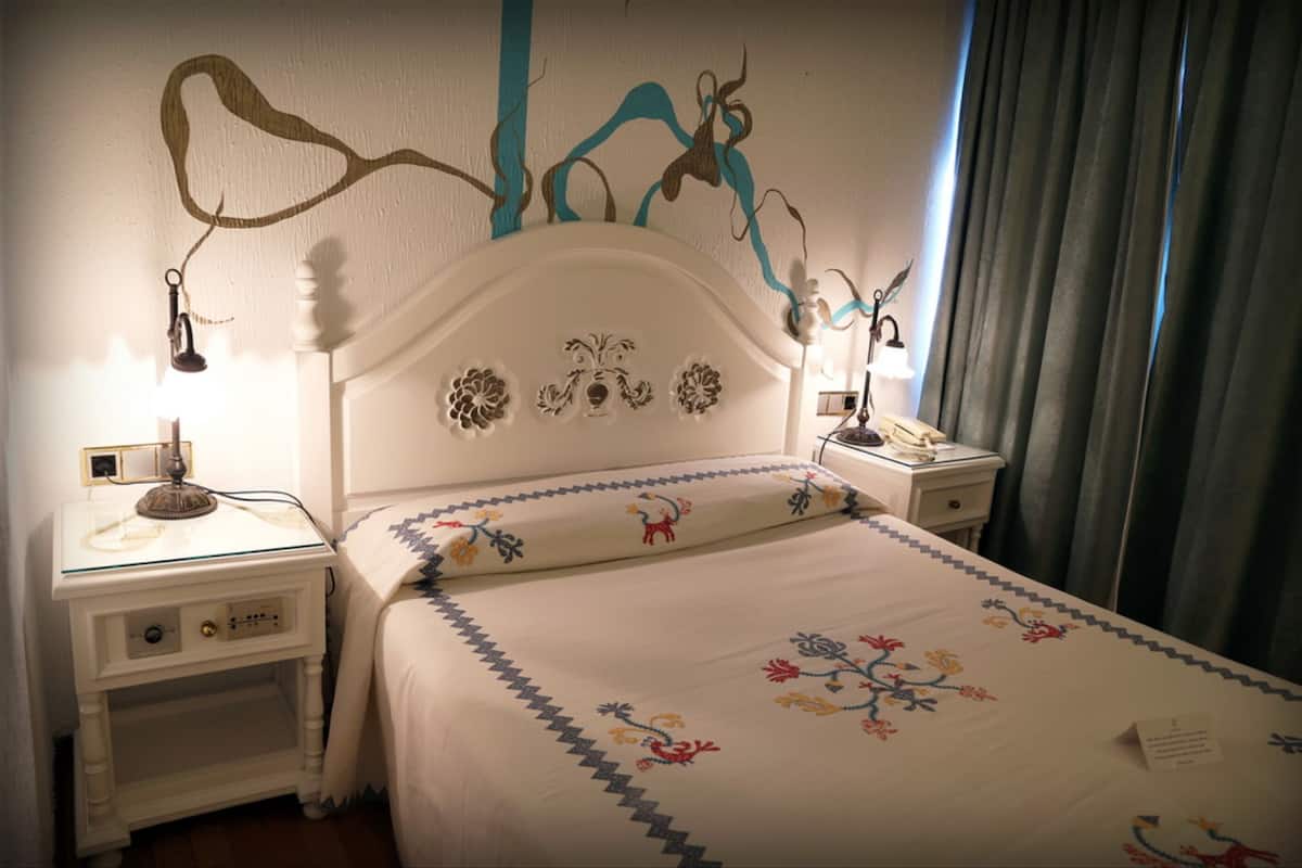 Ein ordentlich bezogenes Bett mit einem blumigen Überwurf, ein weißer Bettrahmen mit Verzierungen und Nachttischlampen auf Nachttischen.
