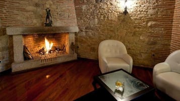 A room with a stone fireplace, wooden flooring, and white leather armchairs.