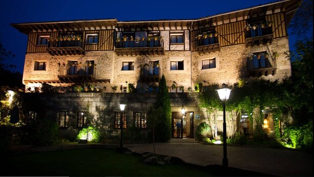 A multi-story building with stone walls and wooden balconies, featuring outdoor lighting and greenery. - Hotel Doña Teresa (La Alberca)