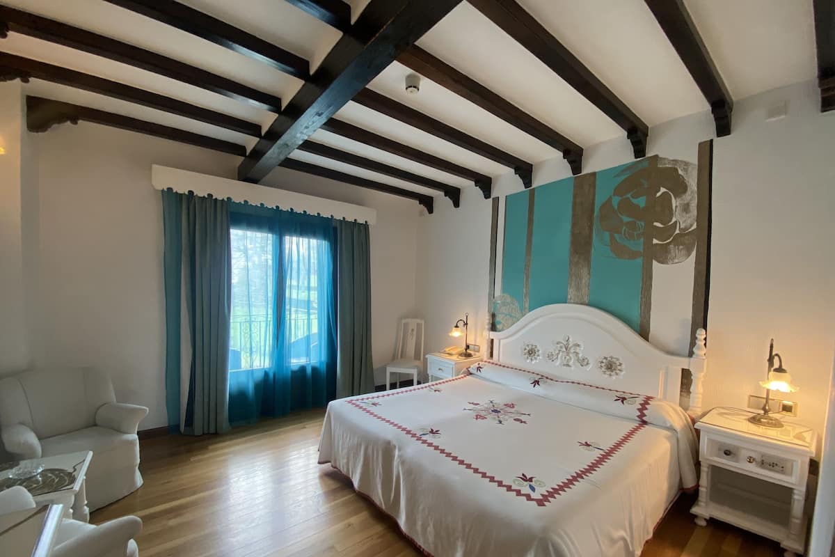 Ein Schlafzimmer mit einem großen Bett, einem Sessel, einem Nachttisch und einem Fenster mit Vorhängen.