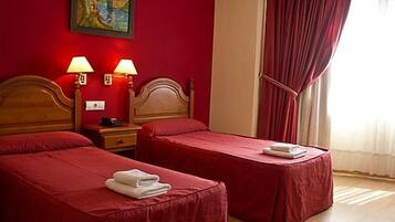 A hotel room with two single beds, red walls, a painting, and a window with red curtains.