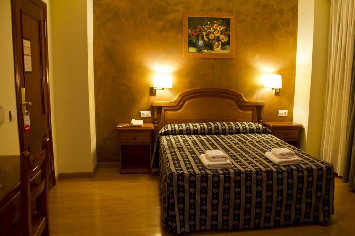 A hotel room with a large bed, two bedside lamps, a nightstand, a wooden door, and a painting on the wall.