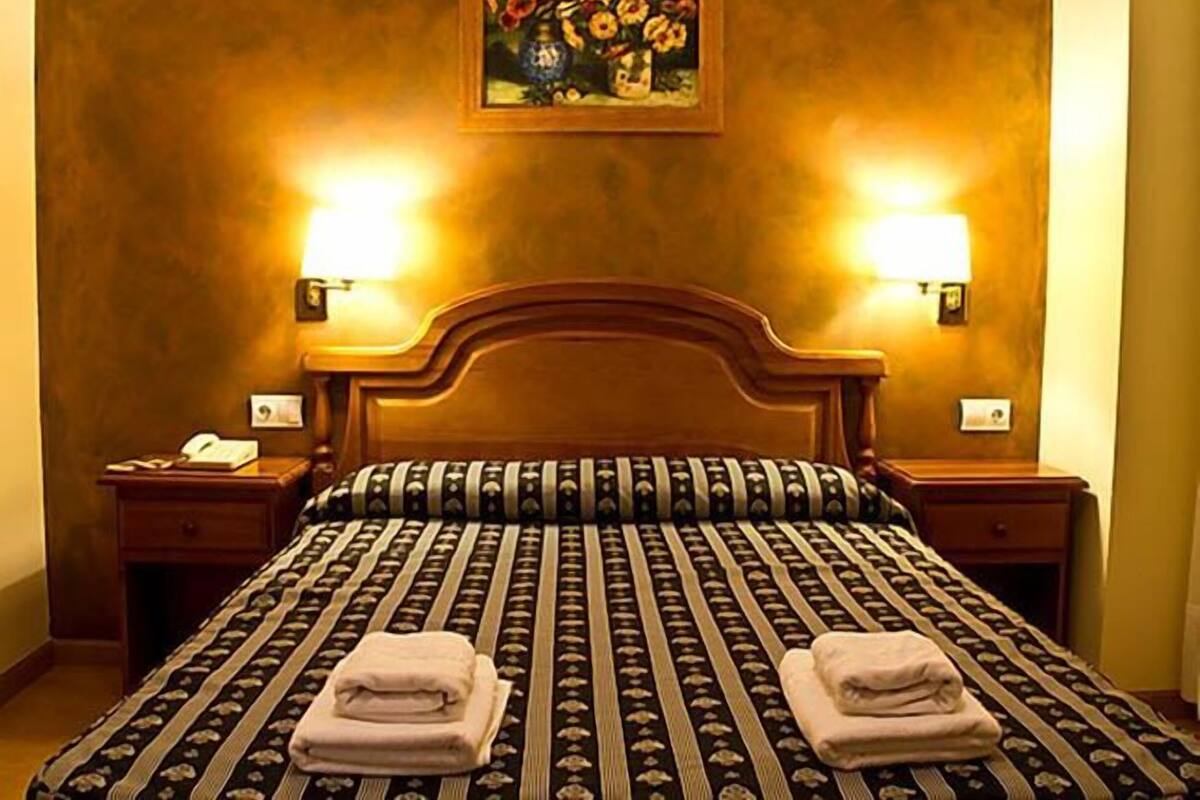 A hotel room with a large bed, two bedside lamps, a nightstand with a phone, and a painting on the wall.