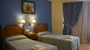 A hotel room with two single beds, a nightstand with a lamp, a painting on the wall, and a window with curtains. - Hotel Clemente (Barbastro)