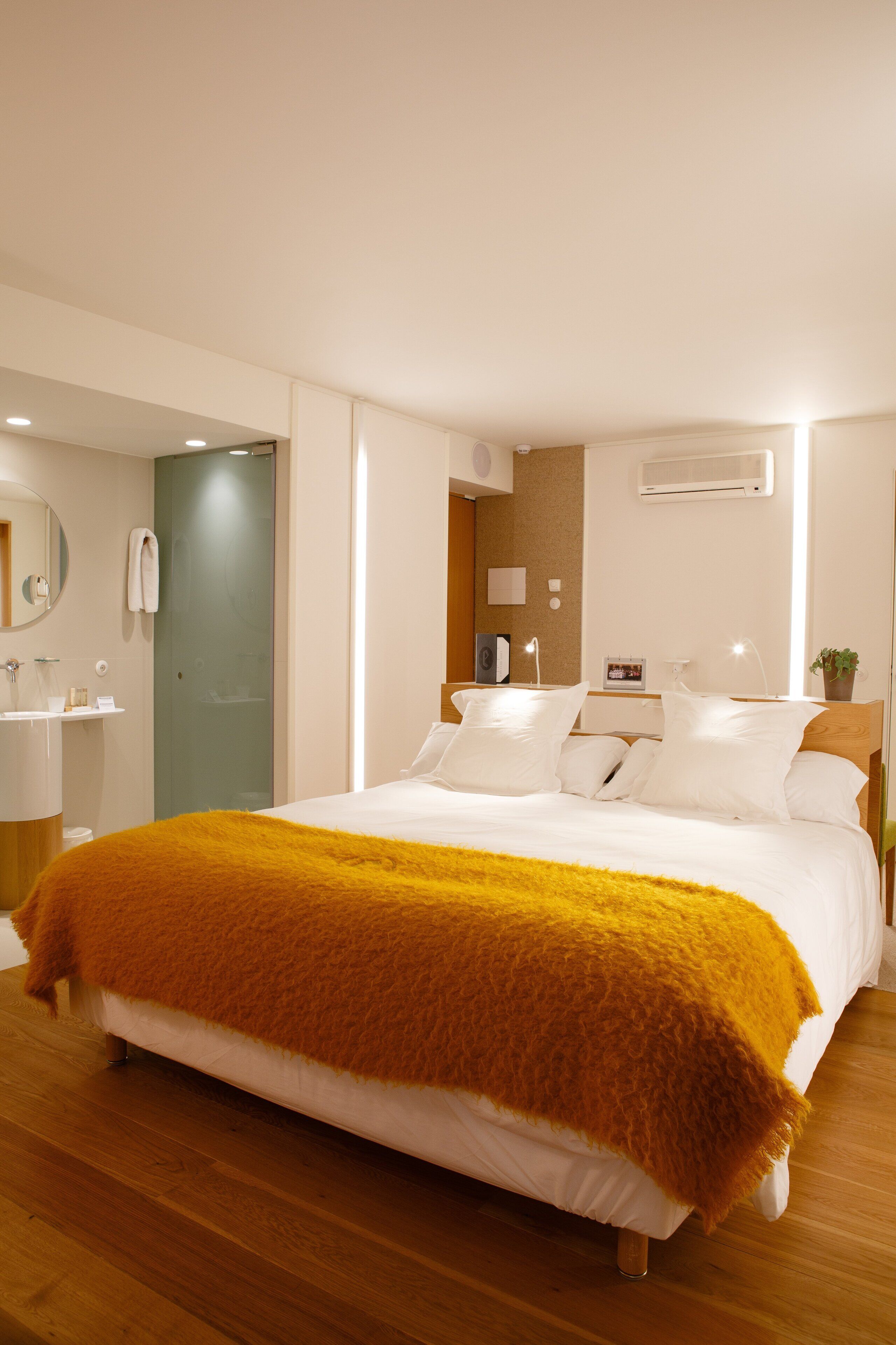 Habitación de hotel moderna con una cama grande, baño con lavamanos y espejo, y acceso a una zona de ducha.