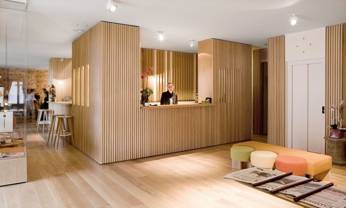 A modern reception area with a wooden reception desk, a seating area with colorful cushions, and a visible staircase leading to another floor.