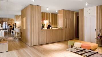 A modern reception area with a wooden reception desk, a seating area with colorful cushions, and a visible staircase leading to another floor.