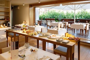 Un espace repas avec des tables préparées pour le petit-déjeuner, proposant une variété d’aliments et de boissons, et offrant une vue sur la verdure environnante.
