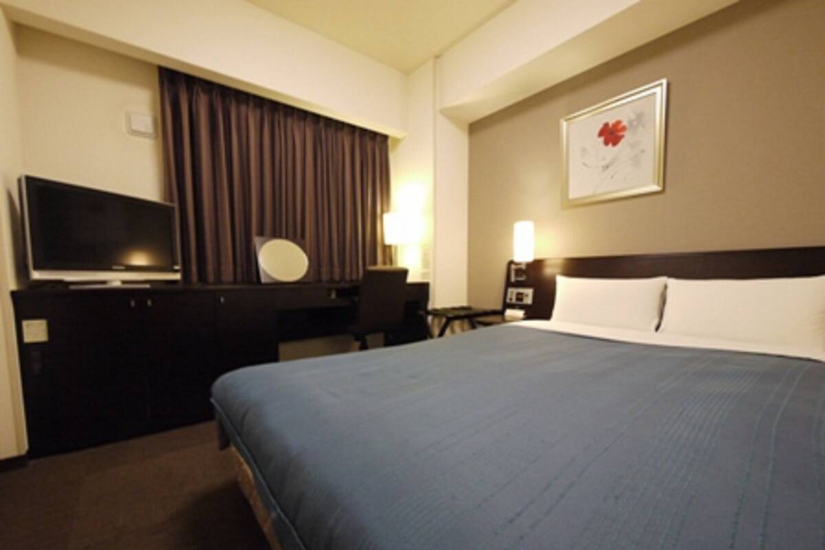 A hotel room with a large bed, a desk with a chair, a television, and a wall-mounted artwork.