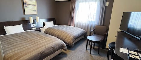 Habitación de hotel con dos camas, un escritorio con televisor, una silla, una mesita y un ventanal con cortinas.