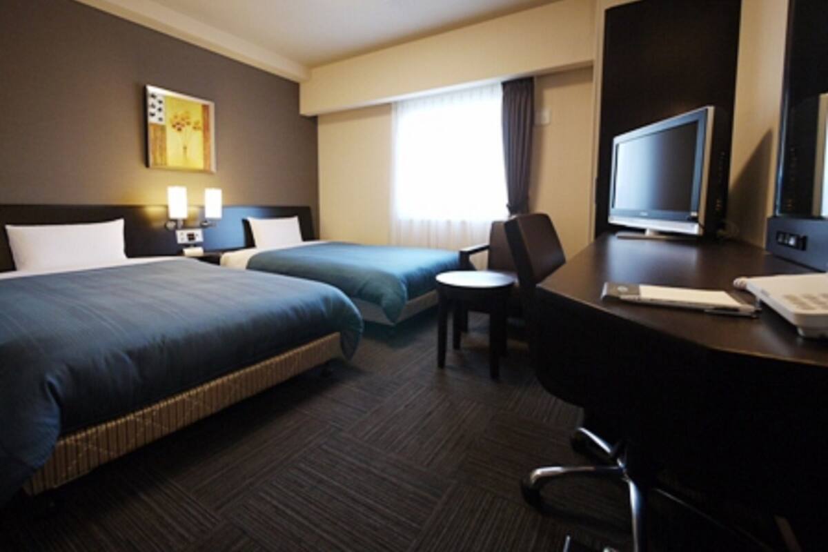 A hotel room with two beds, a desk with a computer, a chair, and a TV.