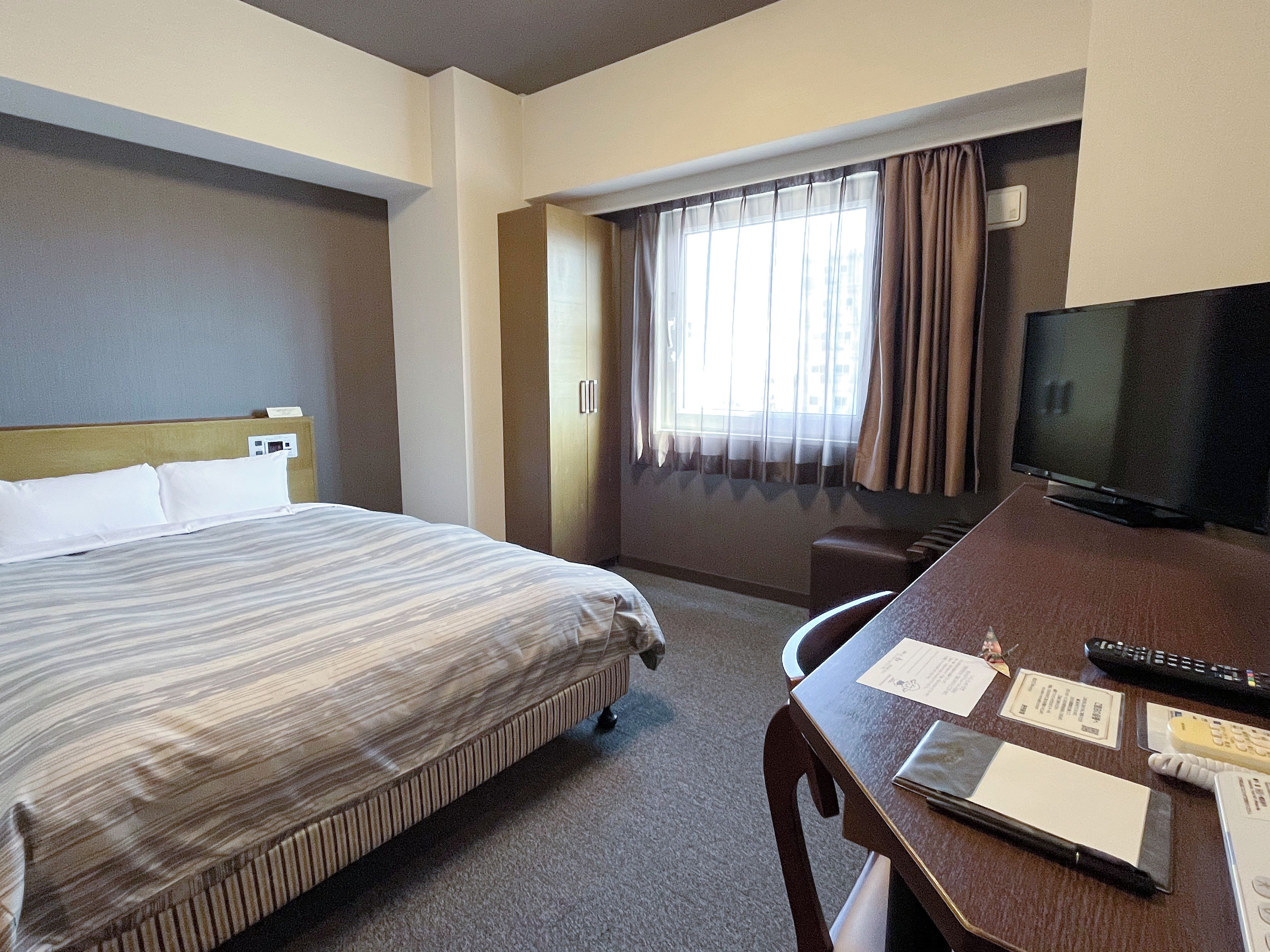 Ein Hotelzimmer mit einem Bett, einem Schreibtisch mit Fernseher und einem Fenster mit Vorhängen.