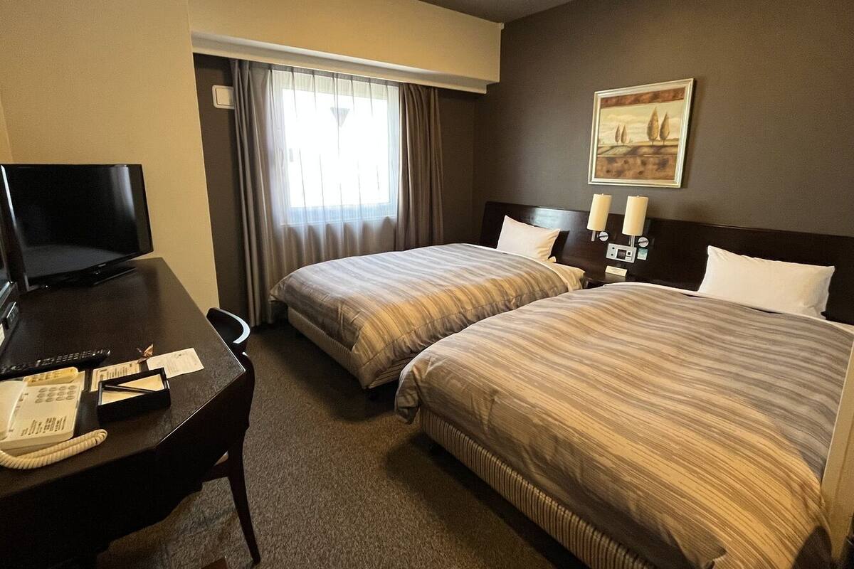 A hotel room with two beds, a desk with a telephone, and a television.