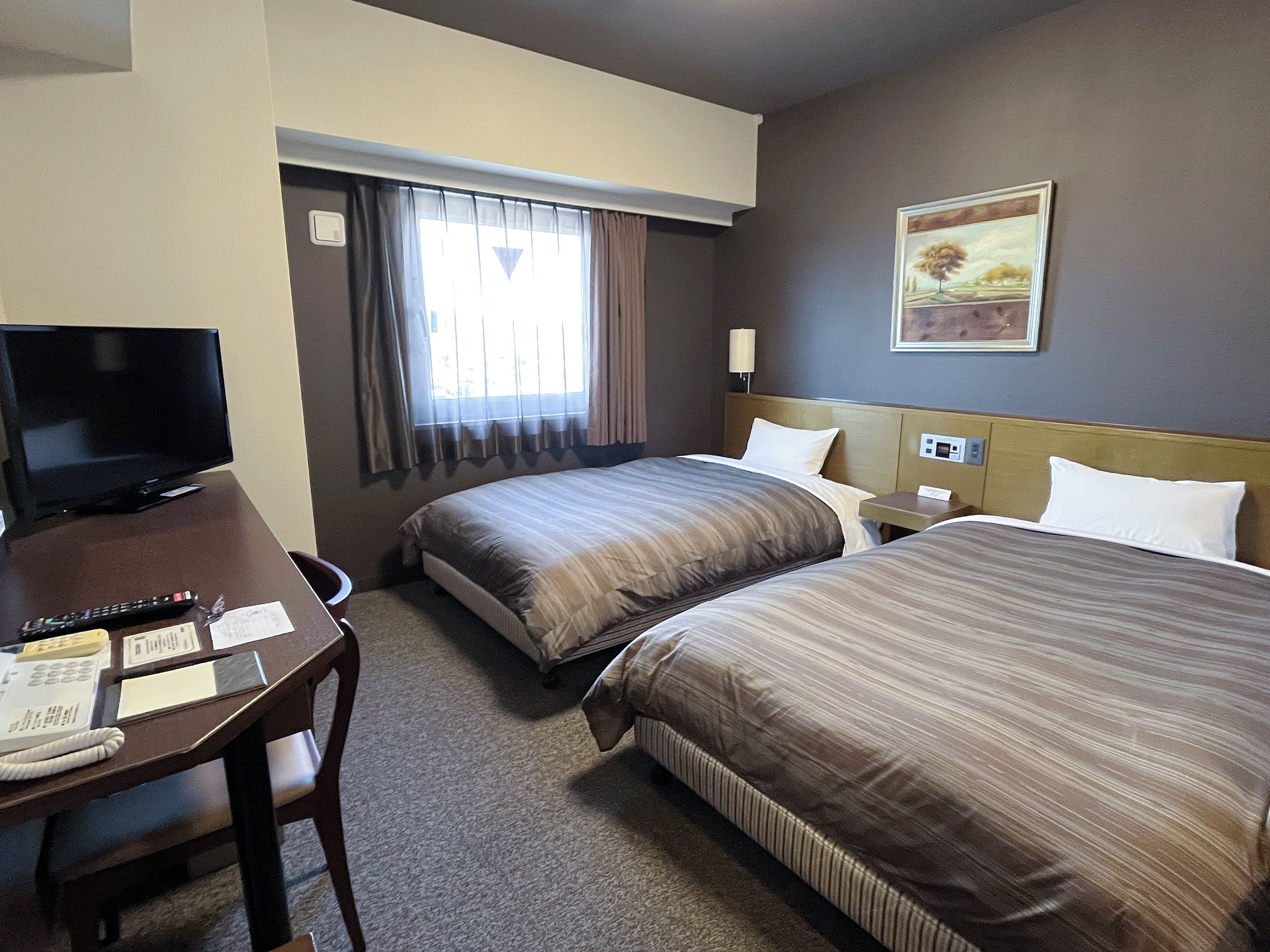 A hotel room with two beds, a desk with a television, and a window with curtains.