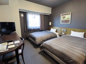 A hotel room with two beds, a desk with a television, and a window with curtains.