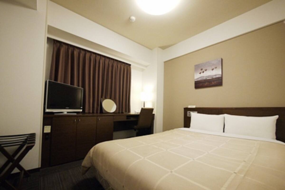 A hotel room with a bed, a desk, a television, and a painting on the wall.