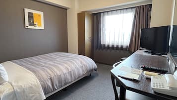 A hotel room with a bed, a desk with a telephone and remote control, a television, and a window with curtains.