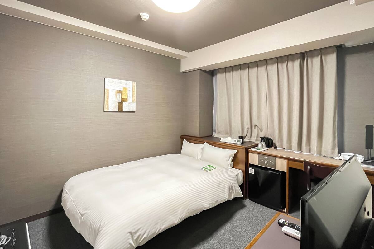 A hotel room with a bed, a desk, a television, and a window with curtains.