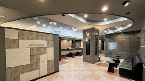 A hotel reception area with a check-in counter, seating area, and a digital information board. - Hotel Route-Inn Dai-Ni Nagano (Nagano)