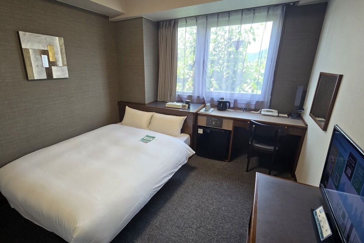 Habitación de hotel con cama, escritorio, silla y ventana con cortinas.