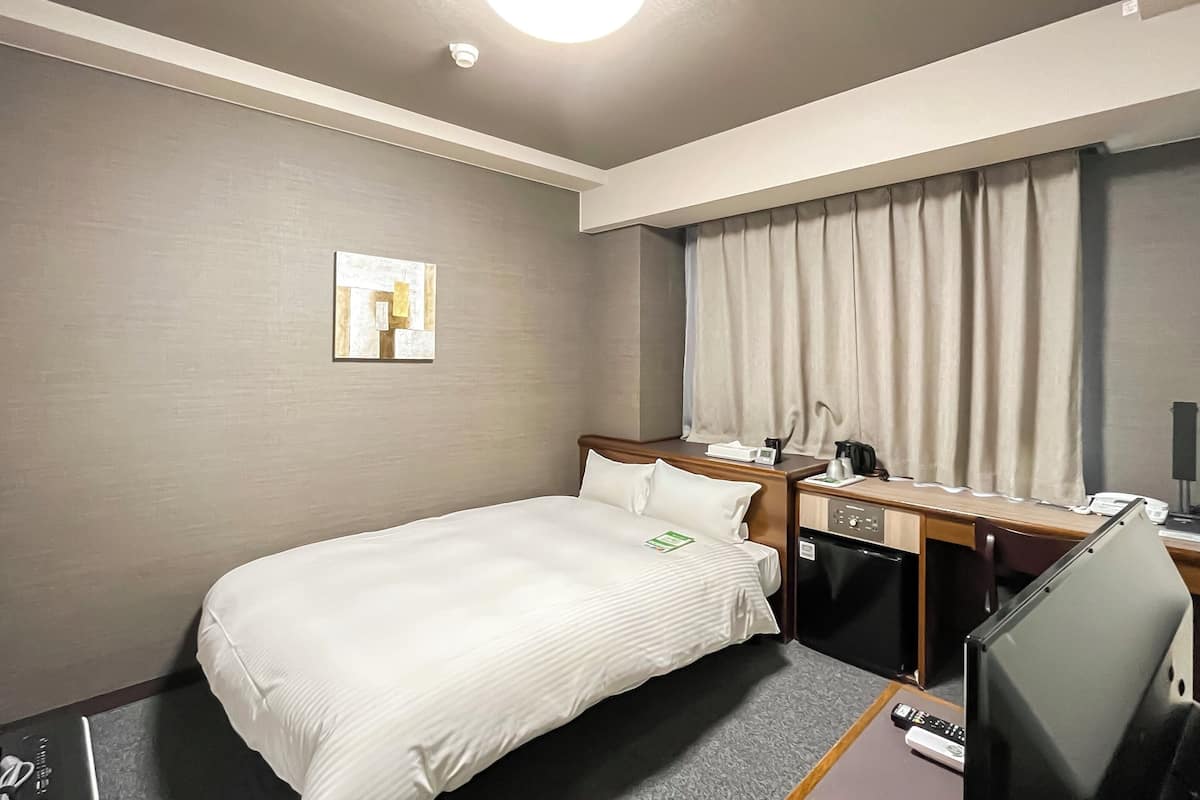 A hotel room with a bed, a desk with a computer, a television, and a window with curtains.