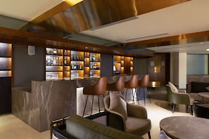 A modern bar area with a marble counter, multiple bar stools, and a seating area with sofas and a round table.