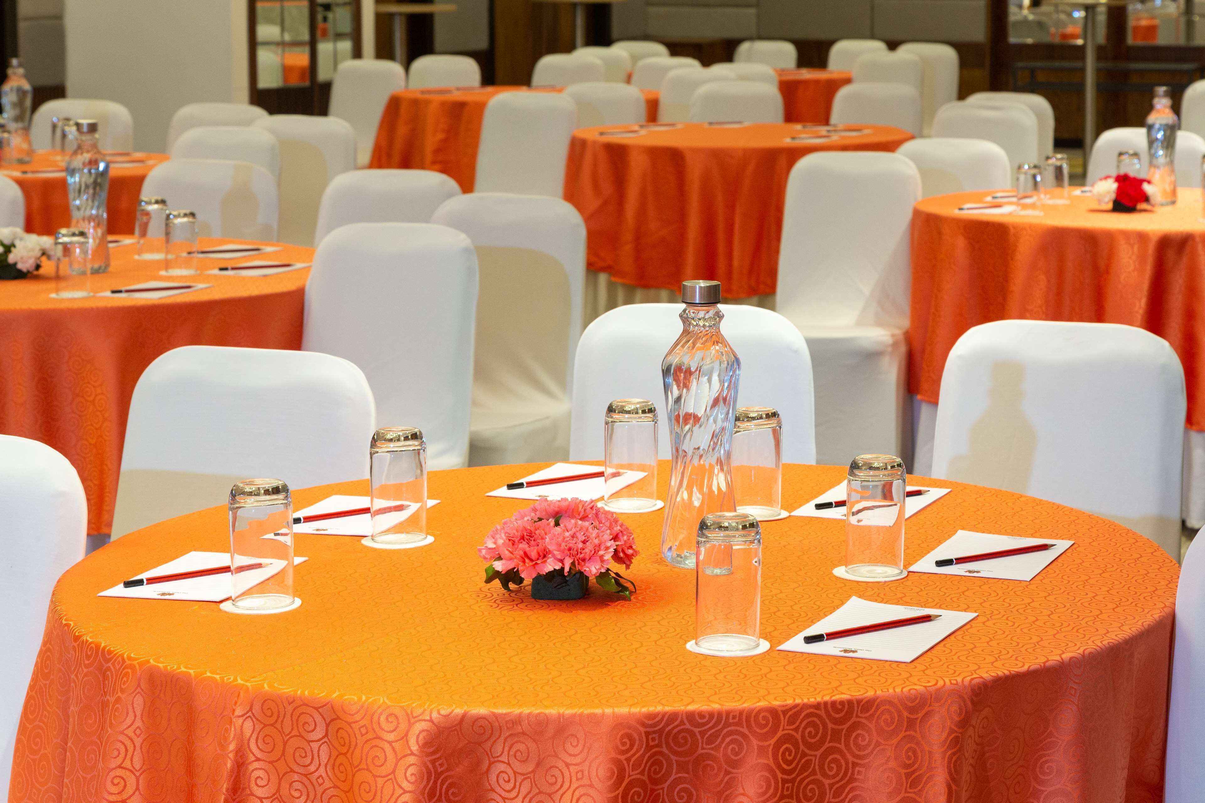 A conference room with round tables, white chairs, and orange tablecloths.
