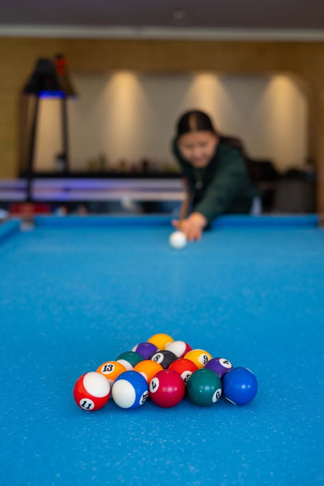 A pool table with a person playing, and a lamp in the background.