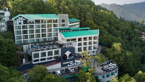 Een modern hotel met meerdere verdiepingen, grote ramen en een groen dak, omringd door weelderige begroeiing en bergen.