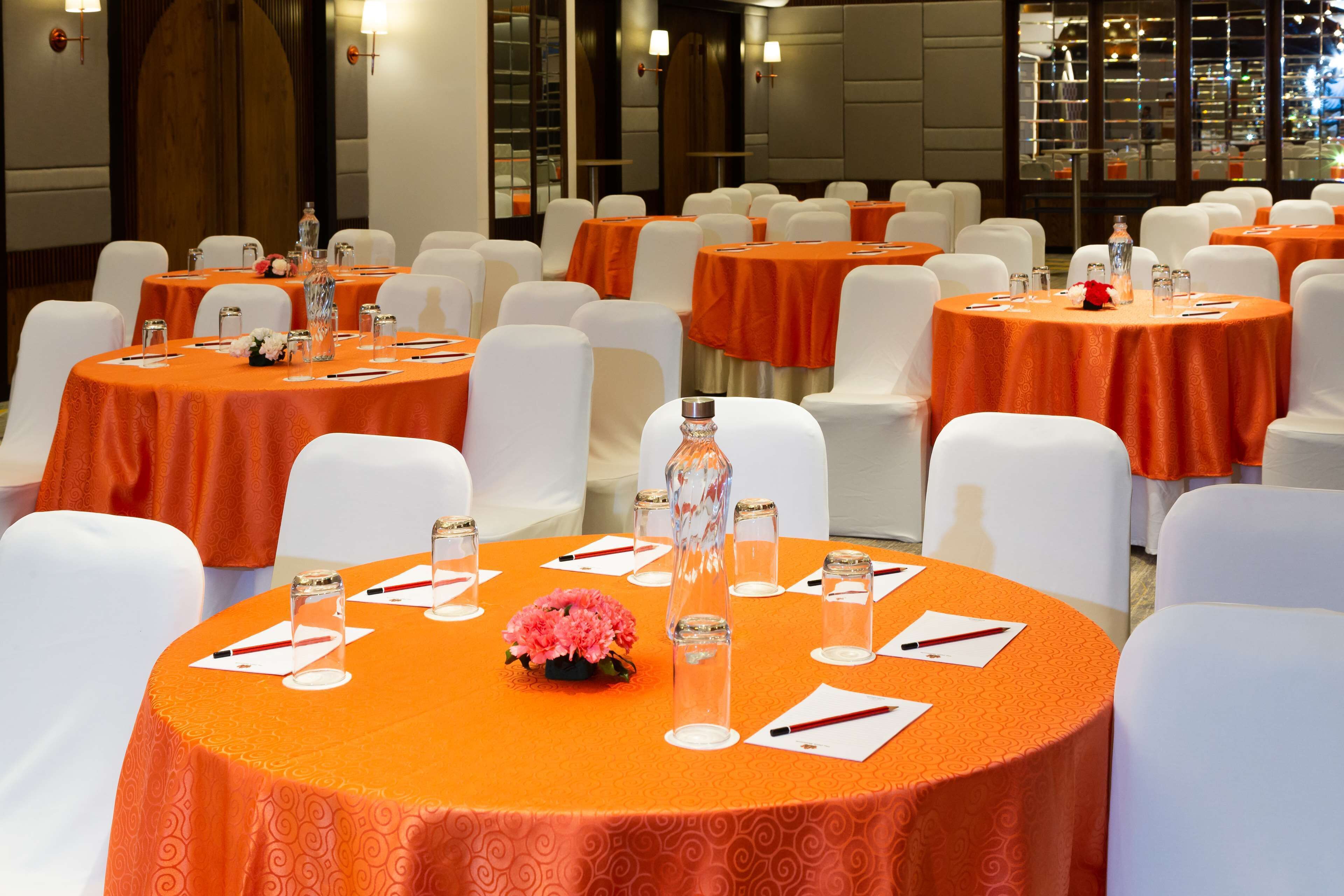 A conference room with multiple tables, each with white chairs, orange tablecloths, and centerpieces.