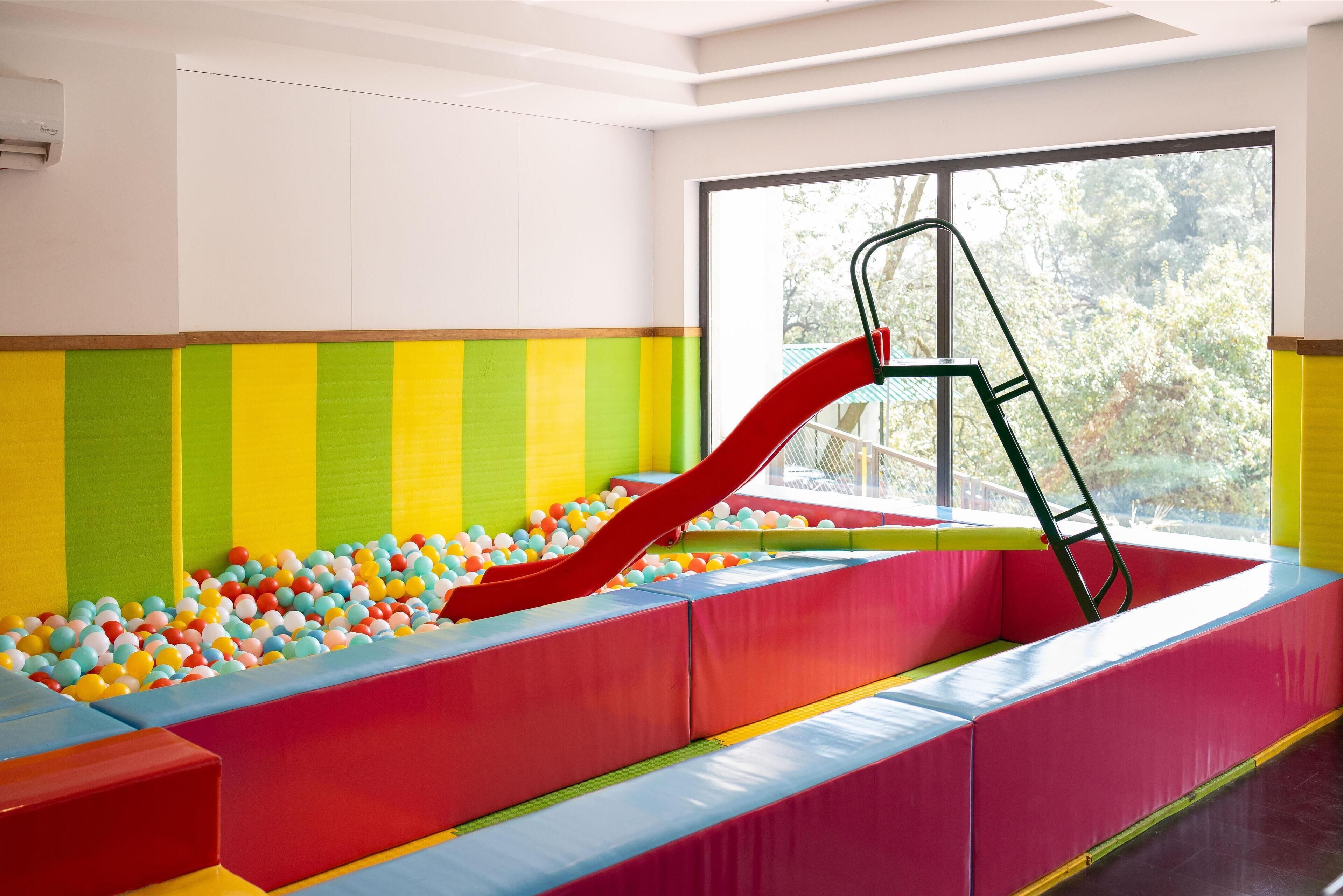 Un área de juegos con un tobogán rojo, paredes acolchadas de colores y una piscina de pelotas.