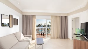 A modern hotel room with a sofa, a small table, a TV, and a balcony with a pool view. - Hotel Riu Paraiso Lanzarote - All Inclusive (Tías)