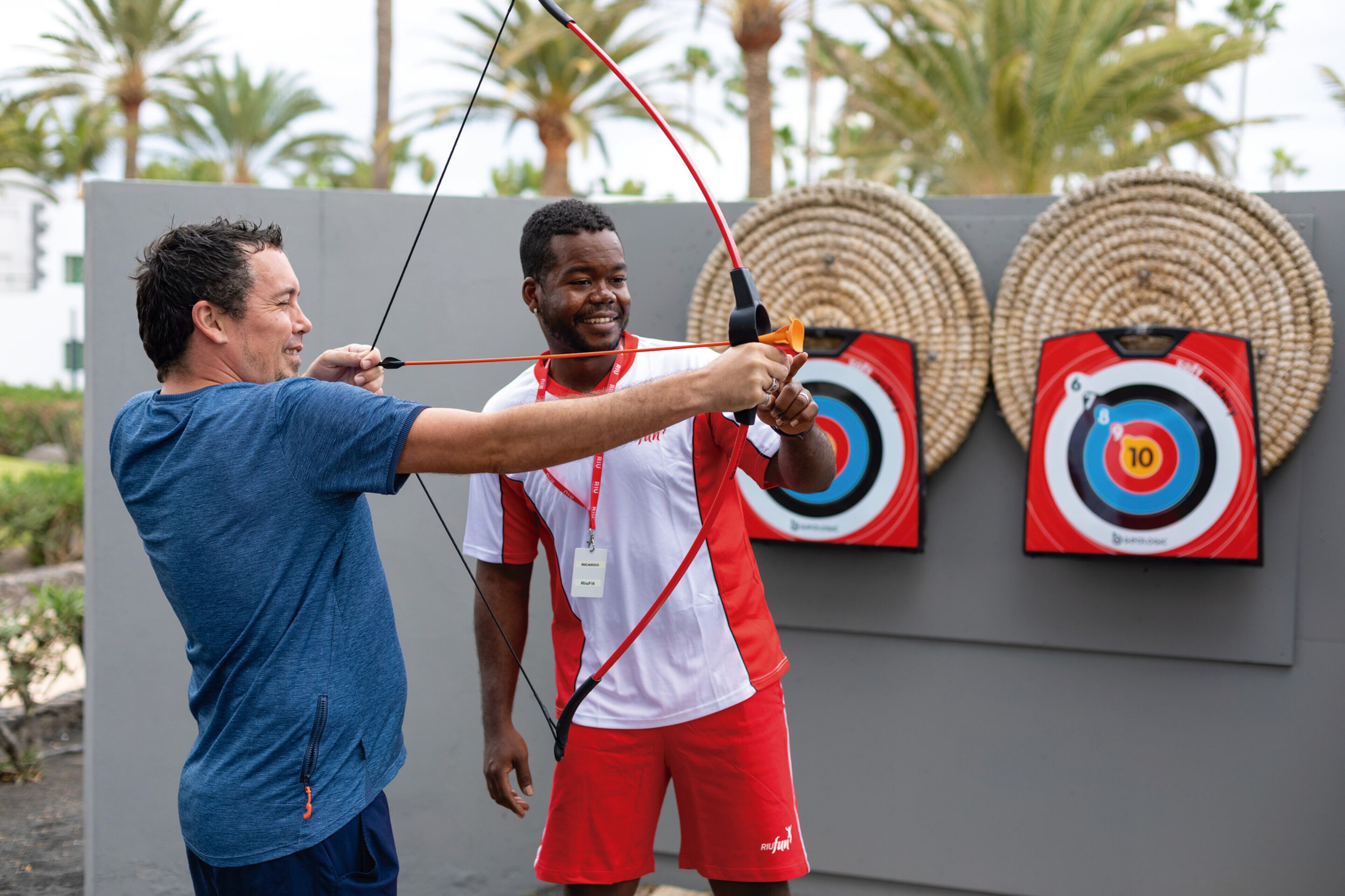 Two people practicing archery with targets in the background.