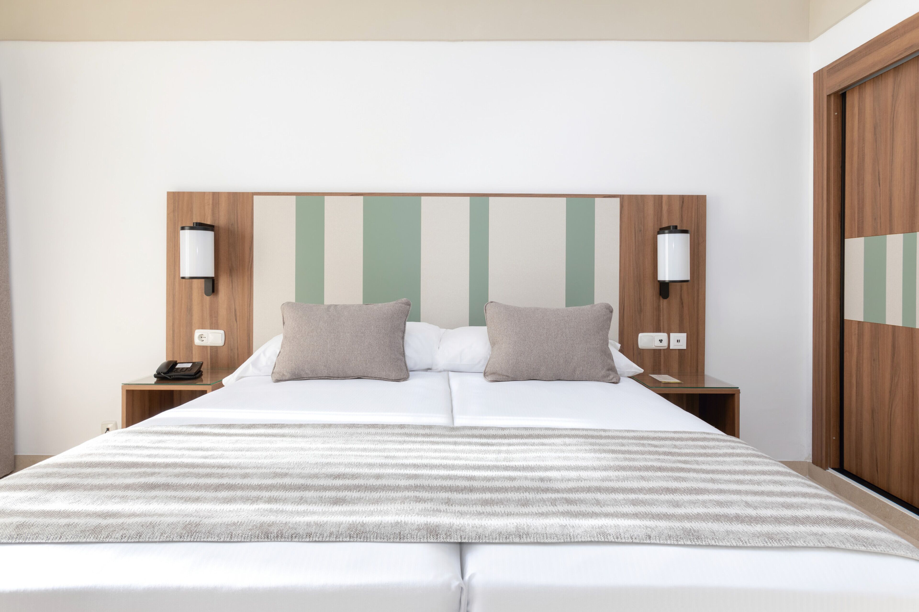 Habitación de hotel con una cama grande, dos mesitas de noche y un cabecero de madera con rayas verticales.